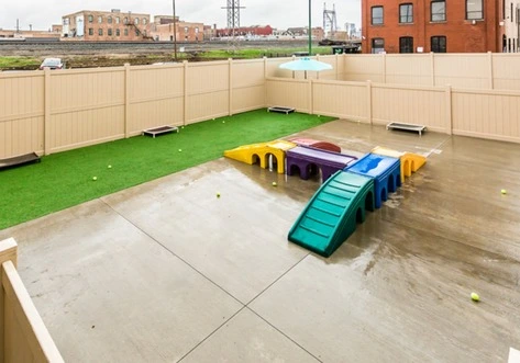A fenced play area with colorful equipment, a slide, and tennis balls on the wet ground.